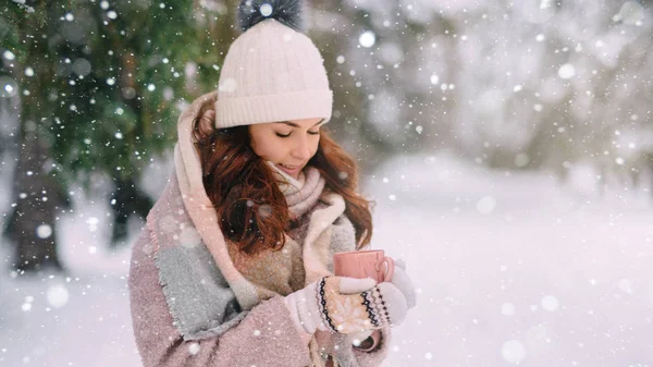 Una joven vestida cálidamente sostiene una taza de bebida caliente en sus manos en un parque de invierno . —  Fotos de Stock