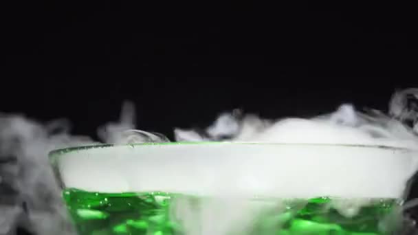 Green liquid boils giving off smoke in a glass bowl on a black background — Stock Video