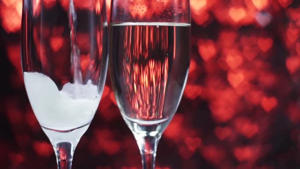 Шампанське наливають у склянку на червоному тлі з багатьма серцями, крупним планом . — стокове відео