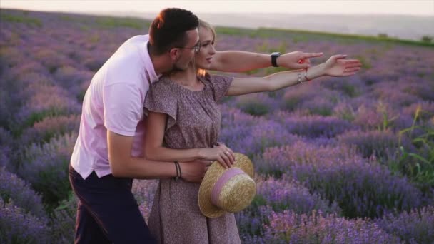 Joven abraza a su novia de pie en un campo de lavanda floreciente — Vídeos de Stock