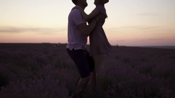 Silhouette Egy fiatalember a karjaiban neveli a barátnőjét, amint egy virágzó levendulamezőn áll napnyugtakor.