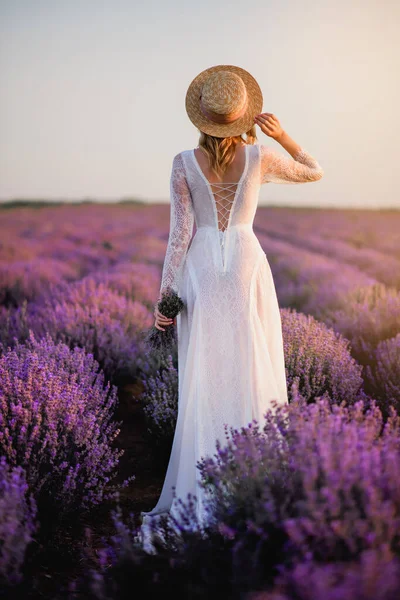 Young woman in white dress walks through blooming lavender field at sunset — Stock Photo, Image