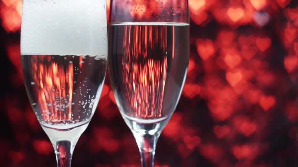 El champán se vierte en una copa sobre un fondo rojo con muchos corazones, de cerca . — Vídeos de Stock