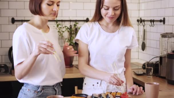 Two funny young lesbians eat sushi rolls at home. — Stock Video