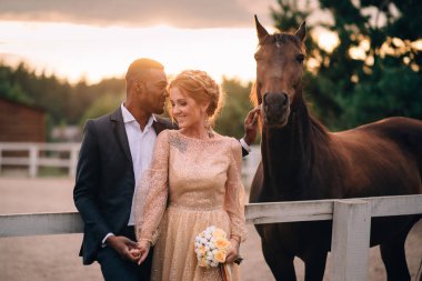 Atlarla çevrili çiftlikte duran mutlu gülümseyen yeni evliler.