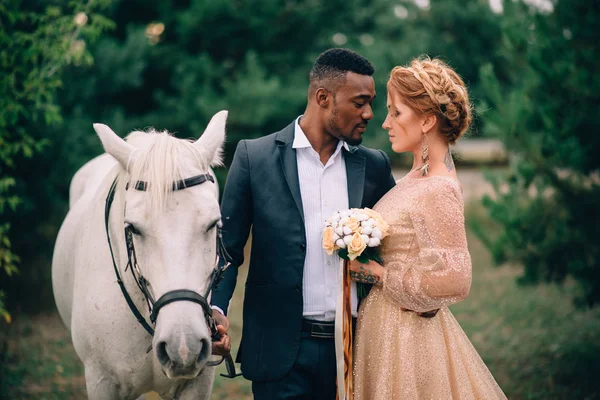 Los recién casados están de pie cerca de un caballo blanco en la naturaleza — Foto de Stock