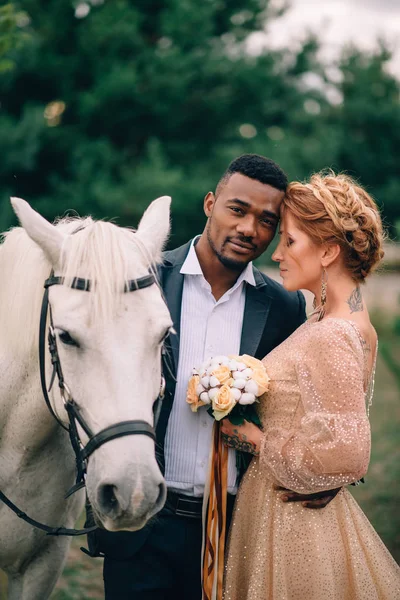 Les jeunes mariés se tiennent près d'un cheval blanc dans la nature — Photo