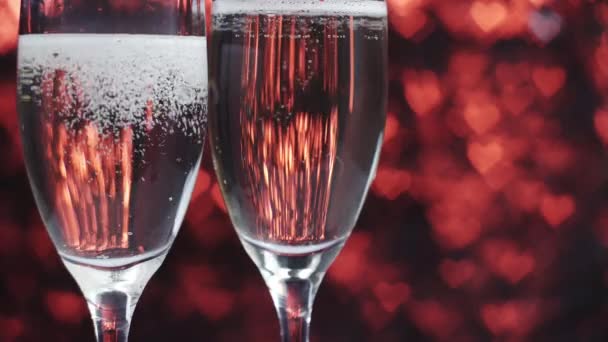 Шампанське наливають у склянку на червоному тлі з багатьма серцями, крупним планом . — стокове відео