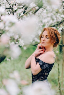 Siyah elbiseli genç bir kadın çiçek açan bir bahçede duruyor..