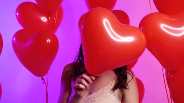 Uma jovem mulher alegre esconde seu rosto atrás de um balão em forma de coração . — Vídeo de Stock