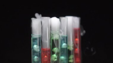 White smoke comes out of test tubes with boiling multi-colored liquid. Close-up.