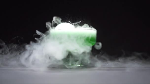 Liquide vert ébullition dégageant de la fumée dans un bol en verre sur fond noir — Video