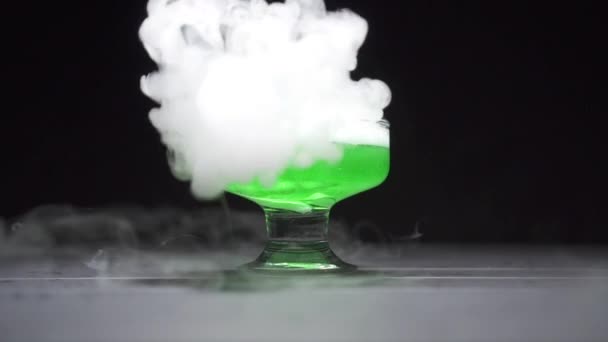 Il liquido verde bolle emettendo fumo in una ciotola di vetro su uno sfondo nero — Video Stock