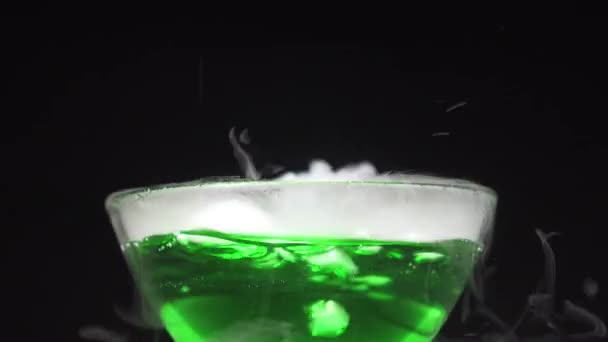 Il liquido verde bolle emettendo fumo in una ciotola di vetro su uno sfondo nero — Video Stock