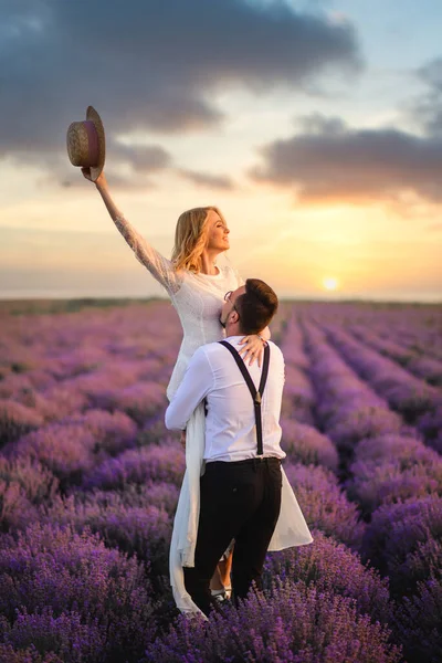 Gelukkige bruidegom houden zijn bruid in zijn armen in bloeiende lavendel veld bij zonsondergang — Stockfoto