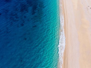 Güzel bir turkuaz denizin kıyılarında beyaz kumlu bir plajın yukarıdan aşağı manzarası..