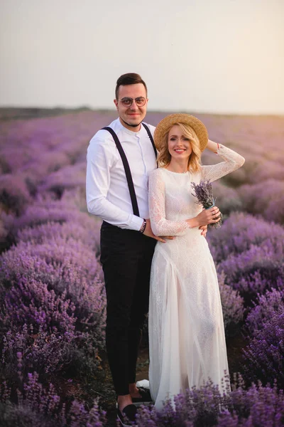 Pareja joven parada en medio del floreciente campo de lavanda al amanecer —  Fotos de Stock