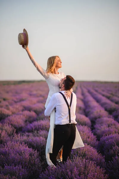 Happy brudgummen håller sin brud i famnen i blommande lavendelfält vid solnedgången — Stockfoto