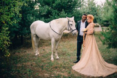 Yeni evliler doğada beyaz bir atın yanında duruyorlar.