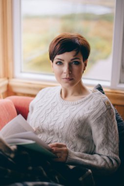 Genç bir kadın evde kitap okuyor..