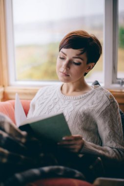 Genç bir kadın evde kitap okuyor..