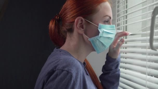 Koruyucu maskeli bir kadın pencereden dışarı bakar.. — Stok video