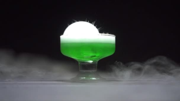 Liquide vert ébullition dégageant de la fumée dans un bol en verre sur fond noir