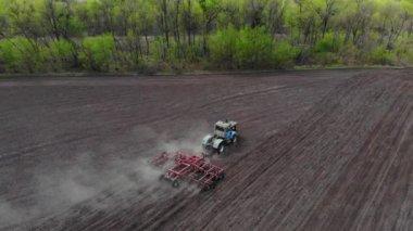 Bir traktör ve tırmık toprağı işliyor..