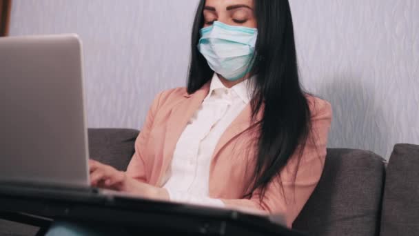 En kvinna i mask arbetar med en dator. — Stockvideo