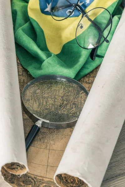 An old colonial map of South America and the flag of Brazil with a magnifying glass and old-fashioned glasses. Vintage style