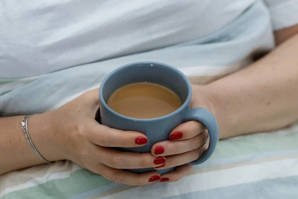 The woman is drinking morning coffee in bed