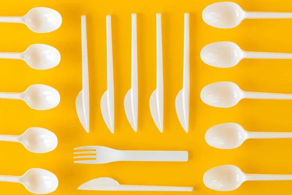 Plastic disposable cutlery on a yellow background.  The concept of reducing the amount of artificial materials on earth