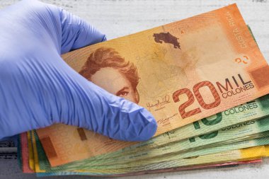  Costa Rica, Colones banknotes kept in rubber gloves. The concept of economy and financial threats during the Coronavirus pandemic clipart