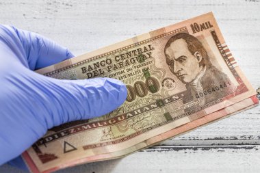 Paraguayan money, Guaranies banknotes kept in rubber gloves. The concept of economy and financial threats during the Coronavirus  clipart