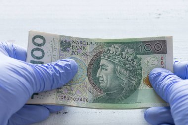 Polonya parası, lastik eldivenlerde tutulan 100 zloti banknot. Coronavirus salgını sırasında ekonomik ve mali tehditler kavramı