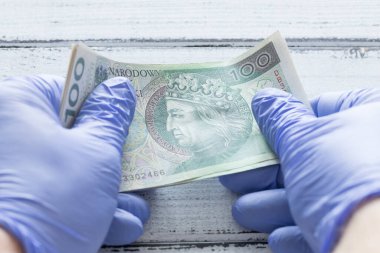 Polonya parası, lastik eldivenlerde tutulan 100 zloti banknot. Coronavirus salgını sırasında ekonomik ve mali tehditler kavramı