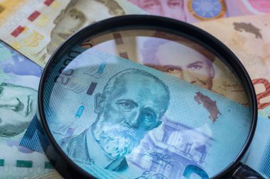Kosta Rika parası, büyüteç altında çeşitli banknotlar. Faiz oranları ve bunların ekonomi üzerindeki etkisi.