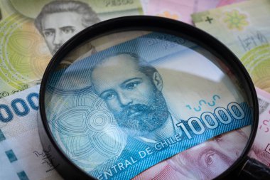 Şili parası, büyüteç altında çeşitli banknotlar. Faiz oranları ve bunların ekonomi üzerindeki etkisi.