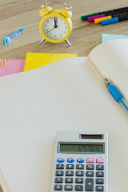 Metin için yeri olan açık bir defter. Alarm saati 12 'ye 5' e ayarlandı. Hesap makinesi, renkli kartlar, kalemler. Ofis kavramı