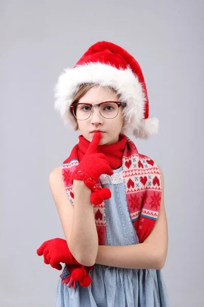 严重的小女孩，在圣诞老人的助手帽子和眼镜在浅色背景的特写肖像 — 图库照片