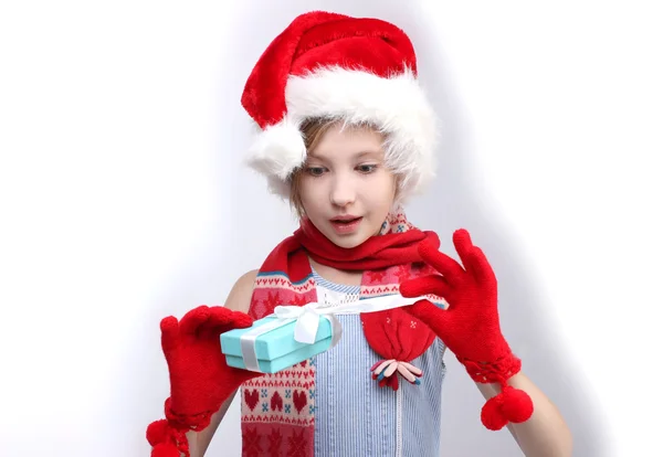 Portrait of little girl in Santa helper hat opening gift boxes over light background — Stock fotografie