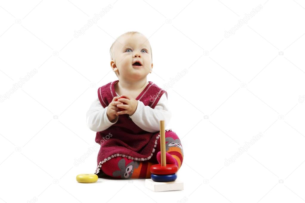 Adorable baby girl in red clothes playing with some  toys, looking up, isolated over white background.