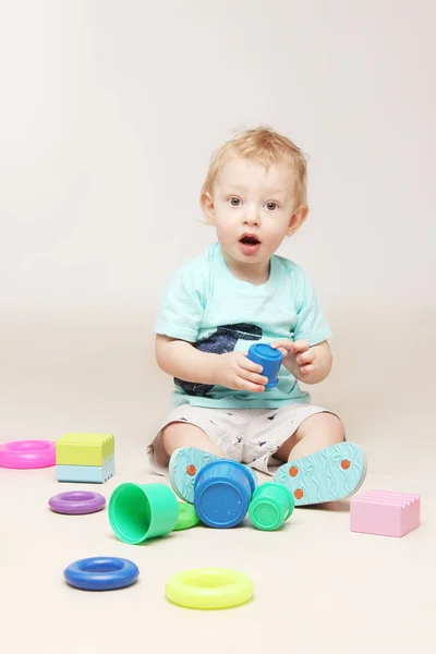 Überrascht Baby Junge sitzt auf dem Boden und spielt mit einigen Spielzeugen. — Stockfoto