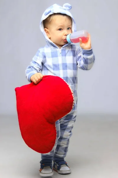 Kleiner Junge steht und hält ein rotes Kissen. — Stockfoto