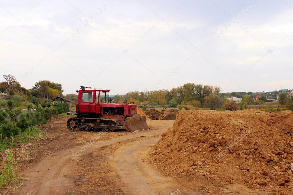 An old red bulldozer outdoors. An excavator stands among gravel, stones and earth in a quarry.