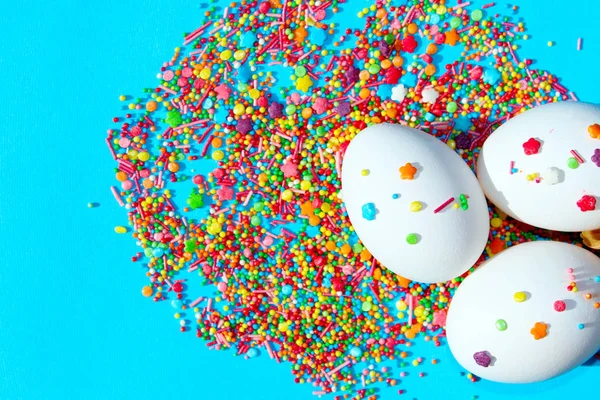 青い背景に3つの白い卵とカラフルなキャンディー イースター フードコンセプト 概要カラフルな食品背景 — ストック写真