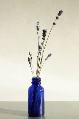 Masanın üzerinde mavi cam şişede lavanta çiçekleri. Çiçekli ve dikey görünümlü soyut arkaplan.