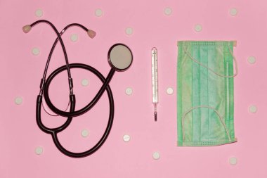 Fonodoskop, maske, beyaz haplar ve pembe arka planda termometre, üst görüş. Sağlık ve Tıp Konsepti.