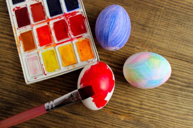 Beyaz tavuk yumurtaları kırmızıya boyanmış, palet renkleri ve ahşap bir masa üzerinde fırça, yatay görüş. Paskalya, tatiller, el yapımı konsept. 