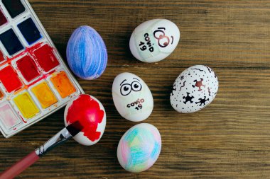 Paskalya, Coronavirus covid-19. Koruyucu maskeli Paskalya yumurtaları ve ahşap arka planda renkli yumurtalar, el yapımı. Paskalya 2020 ve koronavirüs salgını konsepti.